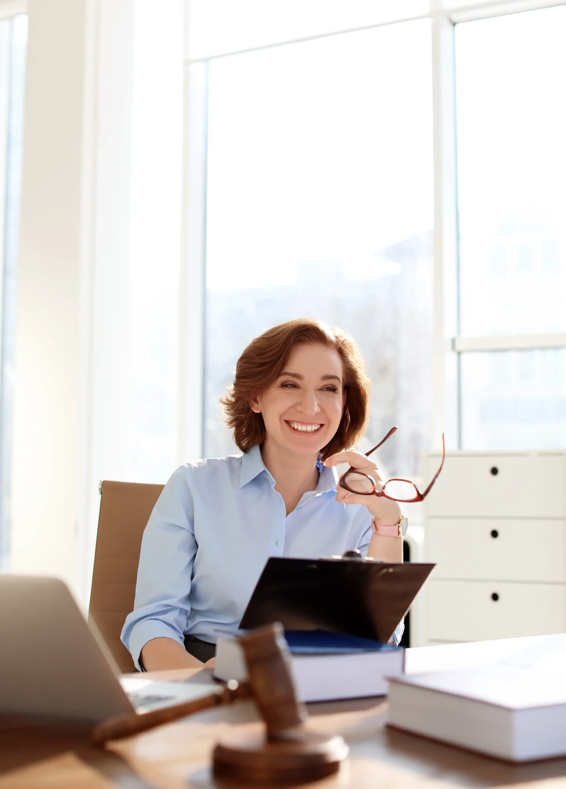A smiling attorney at her desk with a gavel and law books